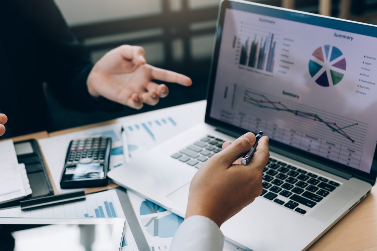Business meeting with graphs on laptop screen.