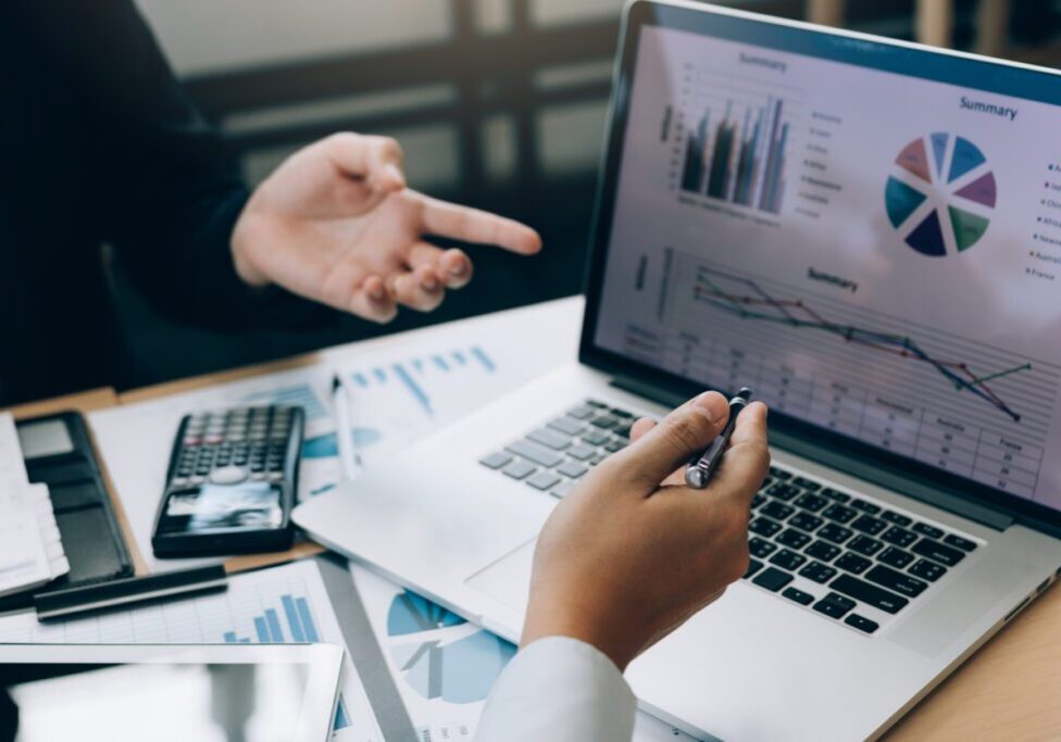 Business meeting with graphs on laptop screen.